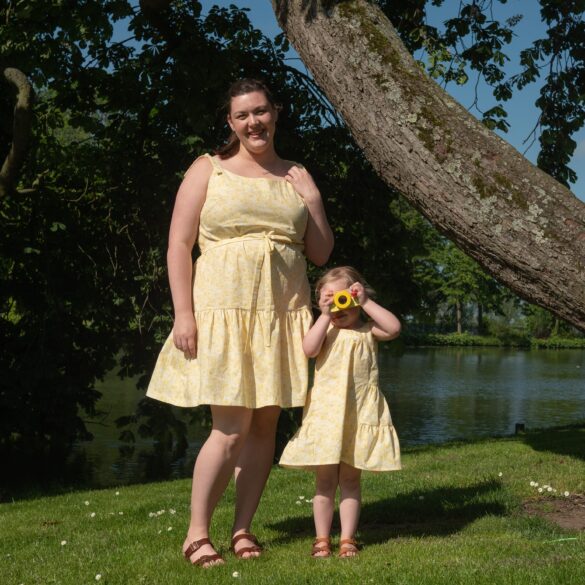 Bri, a white femme and Em a white toddler pose in matching yellow dresses. 